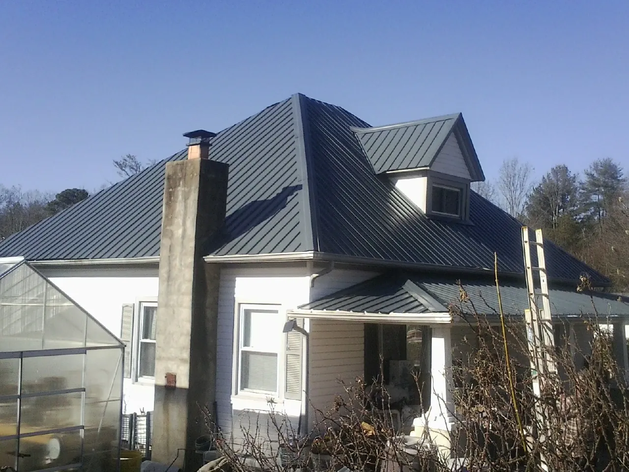 Dark blue standing seam metal roof on a white farmhouse with dormer — Slate & Tile Roof Repair by Roofing Brothers in Mather