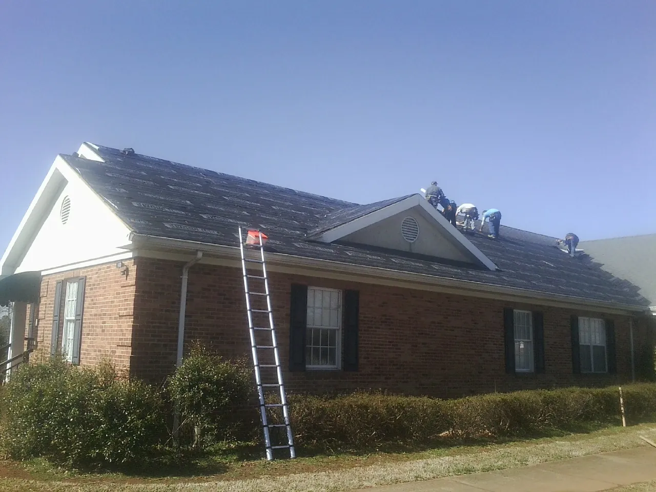 Crew tearing shingles off a brick ranch roof with a ladder set — Metal Roof Repair work by our crew in Mather