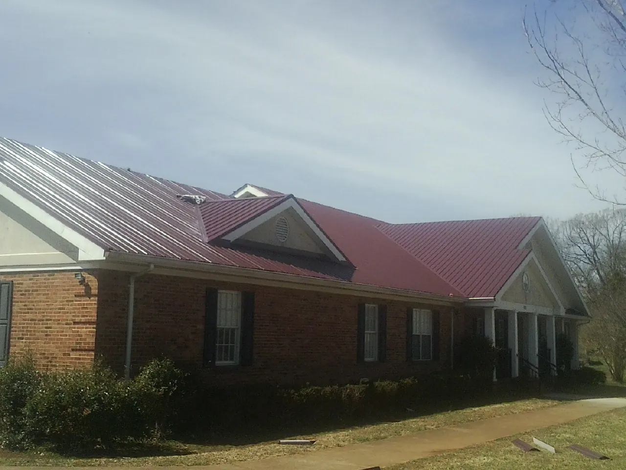 Red metal roof with gabled entries on a long brick building, from a Hail Damage Roof Repair job in Mather