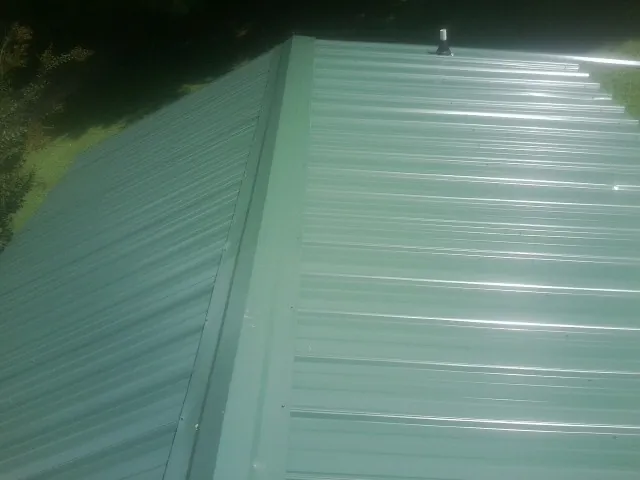New green metal panels meeting at the ridge of a roof — Flat Roof Repair work by our crew in Mather