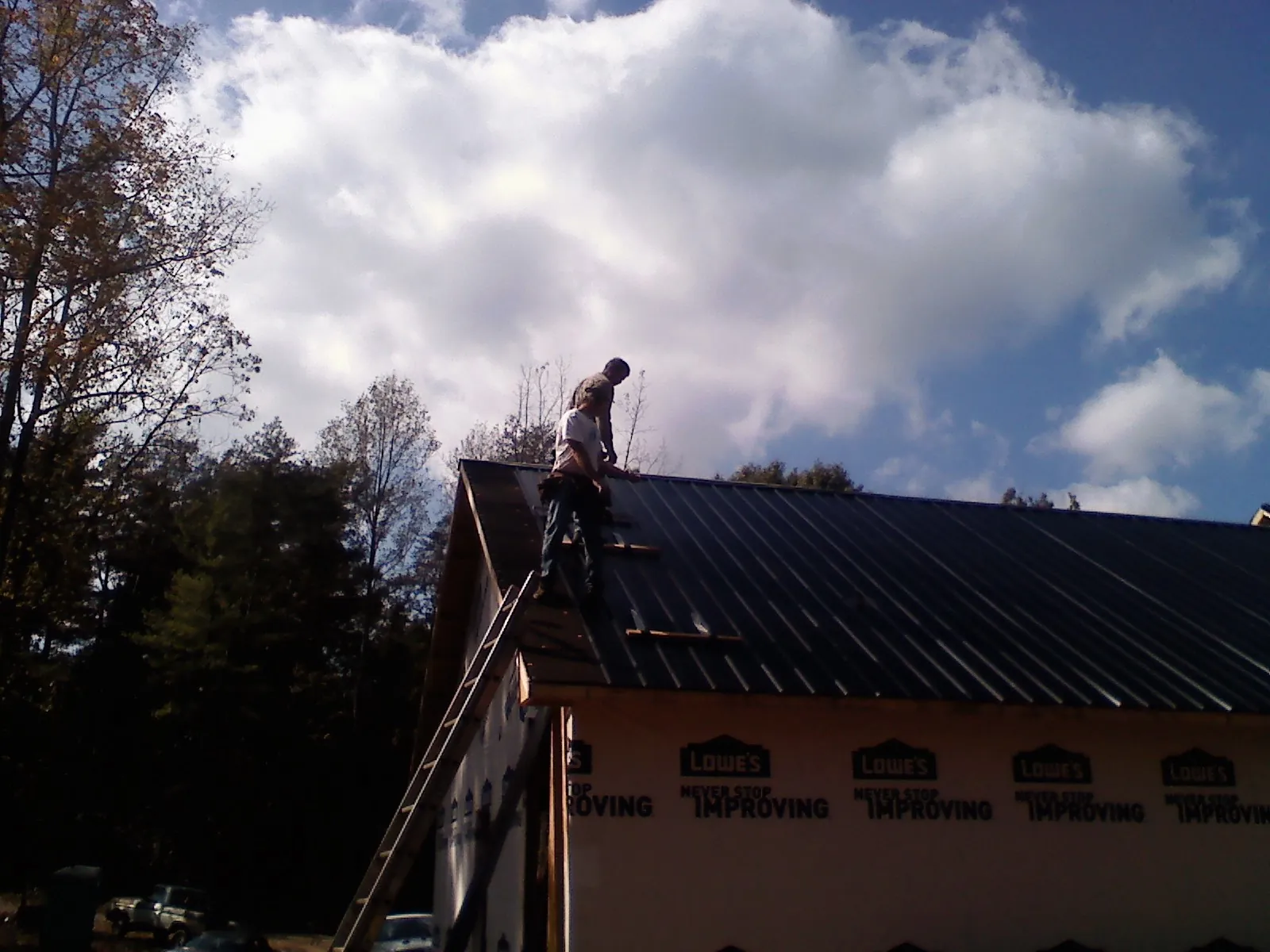 Roofer fastening dark metal panels high against a cloudy sky, from a Roof Inspection job in Mather