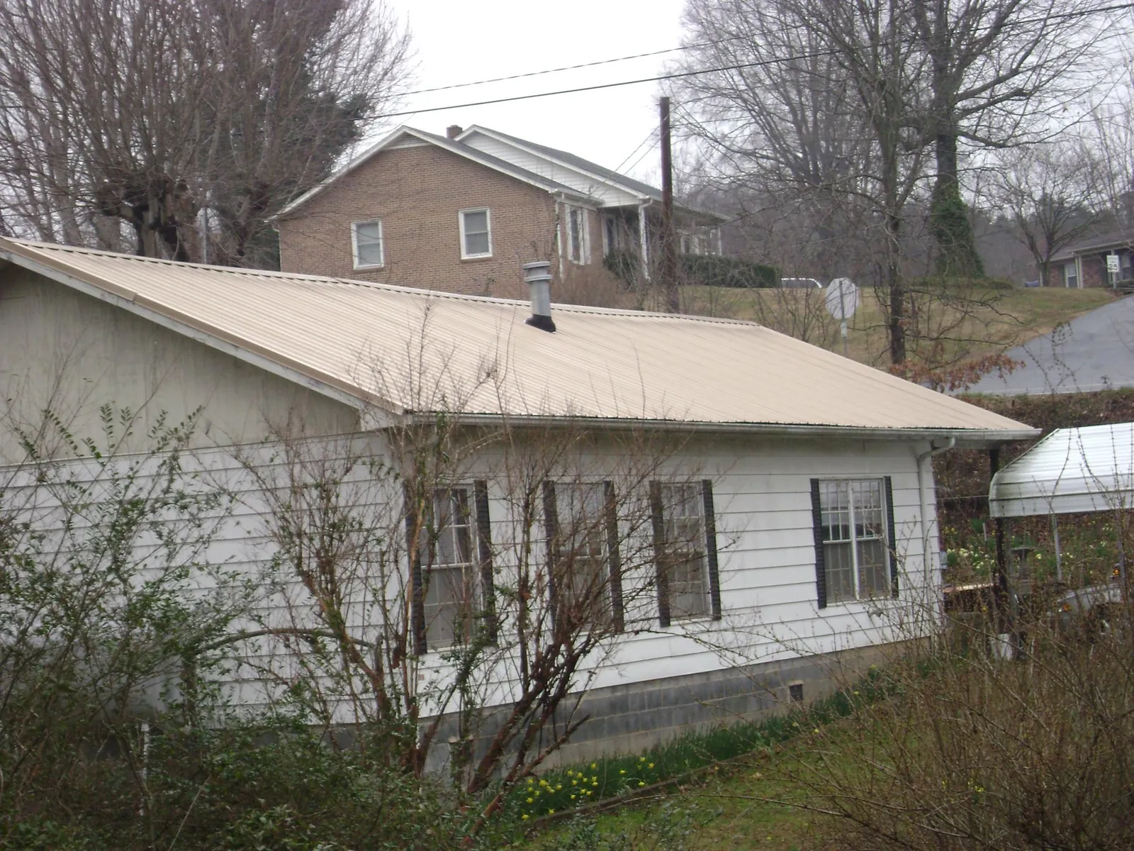 Tan metal roof on a white sided house set into a hillside — Commercial Roofing by Roofing Brothers in Mather
